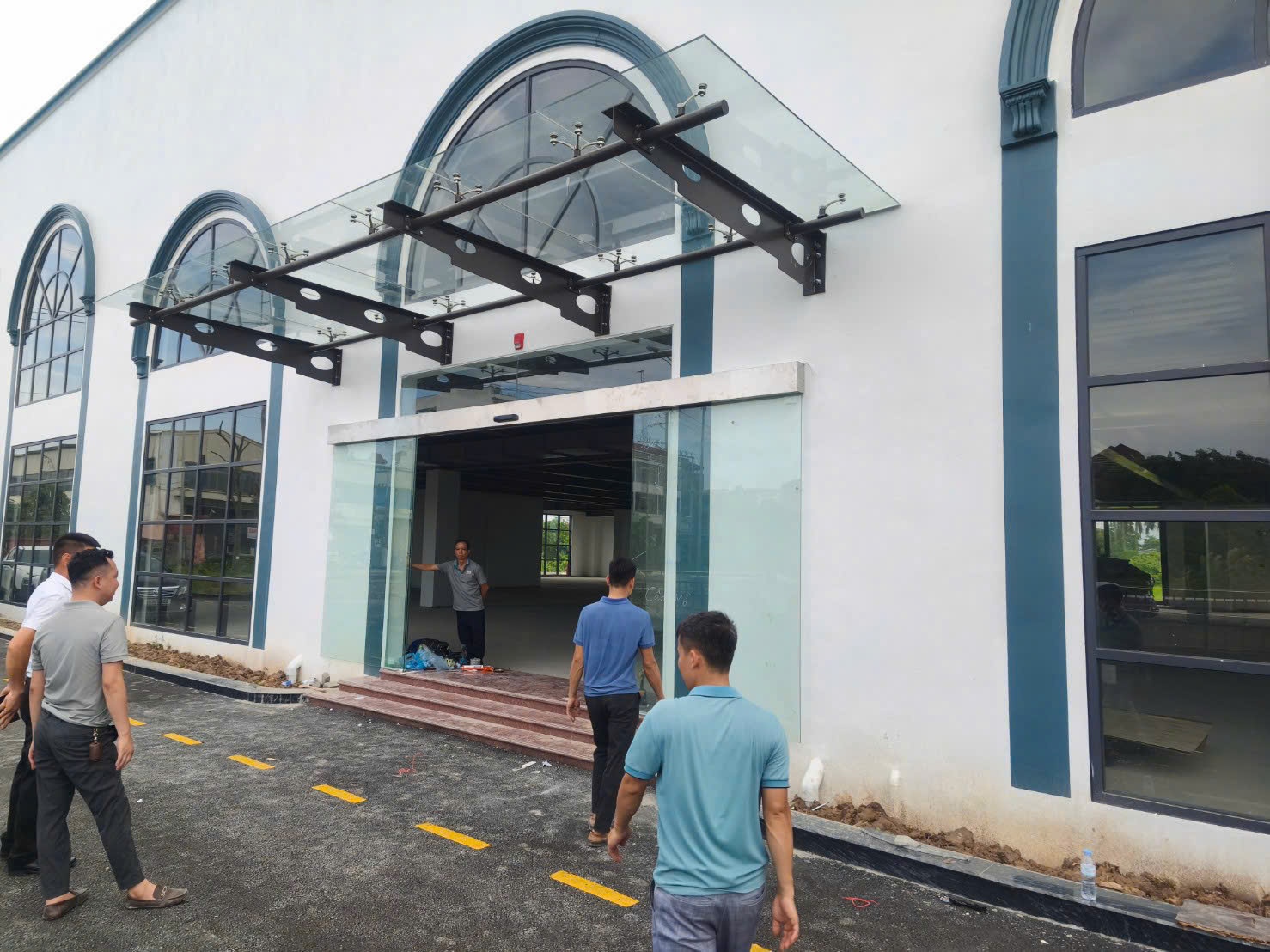 Cửa kính cường lực mặt tiền tòa nhà với mái che kính khung thép, nhóm công nhân đang thi công lắp đặt